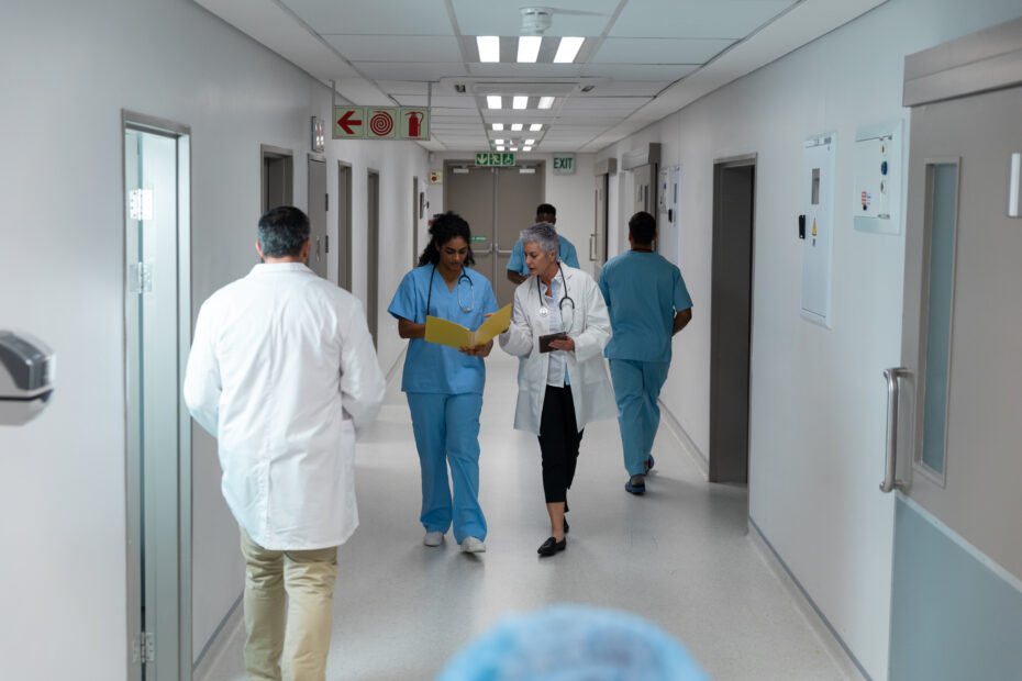 Diverse,Male,And,Female,Doctors,Walking,Through,Hospital,Corridor,Discussing.